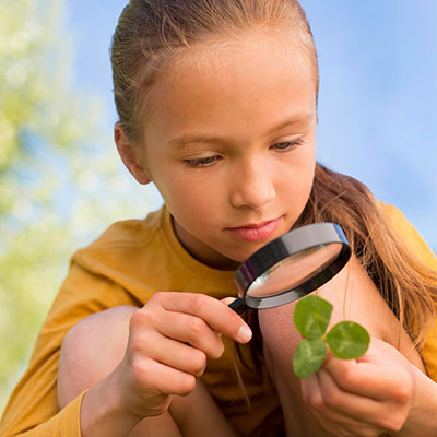 A young girl inspects a clover leaf with magnifying glass.